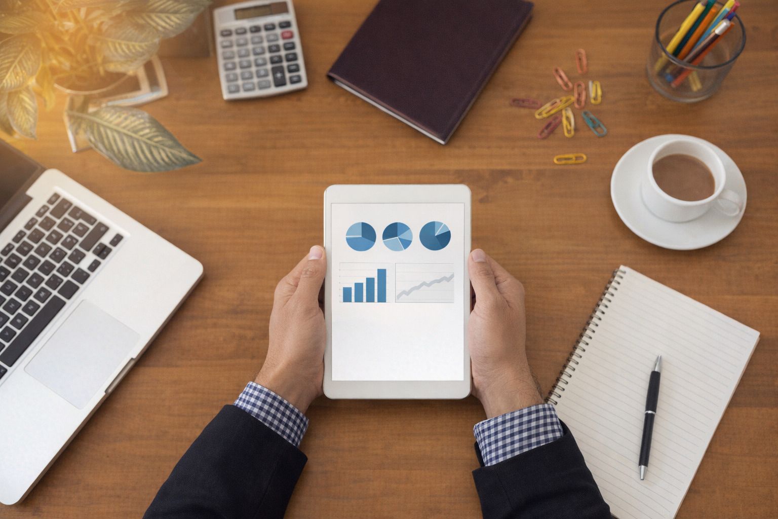 En person granskar finansiella grafer på en surfplatta vid ett skrivbord.